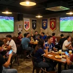 Penggemar yang bersemangat terlibat dalam taruhan judi bola saat menonton pertandingan sepak bola langsung di bar olahraga